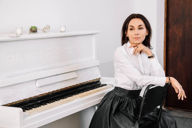 Mulher bonita vestida com camisa branca, tocando piano branco. Lugar para texto ou publicidade