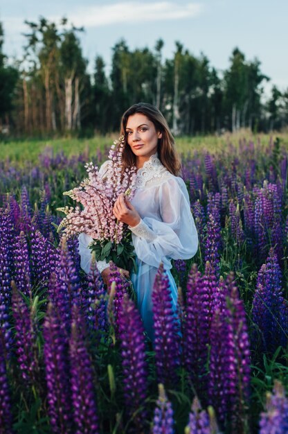 Mulher bonita, vestida com um vestido de tremoço de flores ao pôr do sol