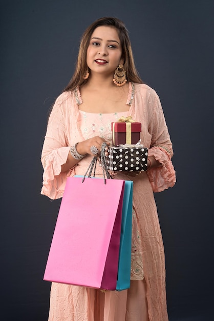 Mulher bonita vestindo vestido tradicional indiano segurando sacolas de compras e caixa de presente em um fundo cinza