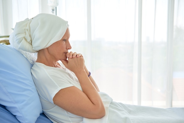 Mulher branca branca sem pêlos e sem sobrancelhas se sentir mal está rezando e esperando por quimioterapia no quarto de hospital, conceito mês de conscientização do câncer de mama.