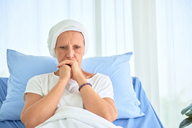 Mulher branca branca sem pêlos e sem sobrancelhas se sentir mal está rezando e esperando por quimioterapia no quarto de hospital, conceito mês de conscientização do câncer de mama.