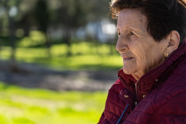 Mulher branca de 90 anos no parque rindo e pensativa.