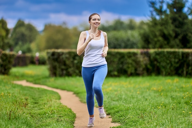 Mulher branca e magra corre em um parque público em roupas esportivas