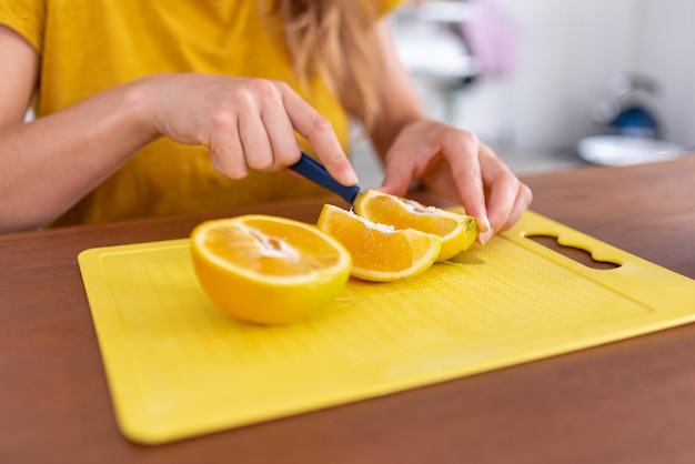 Mulher branca irreconhecível a cortar laranja para um pequeno-almoço saudável.