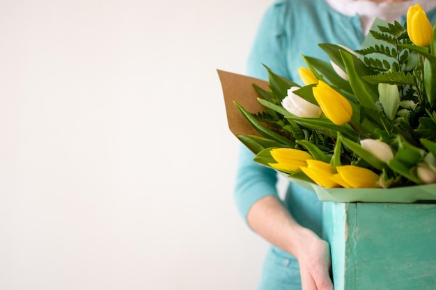 Mulher branca segurando uma caixa rústica turquesa com um buquê de tulipas amarelas e brancas