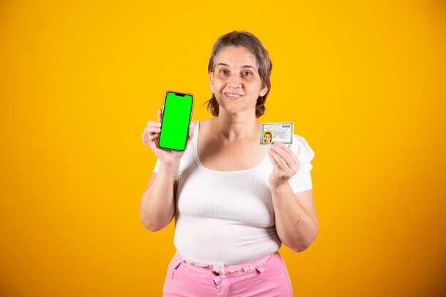 Mulher brasileira adulta segurando carteira de identidade e smartphone com tela verde