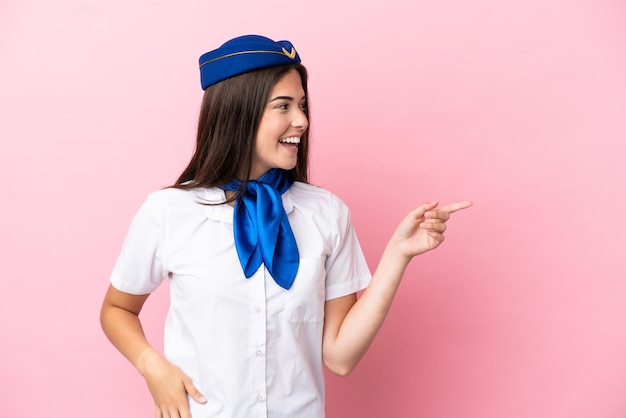 Mulher brasileira aeromoça isolada em fundo rosa apontando o dedo para o lado e apresentando um produto