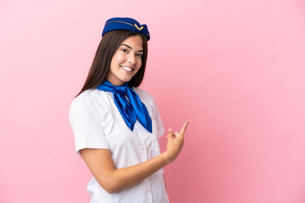 Mulher brasileira aeromoça isolada em fundo rosa apontando para trás