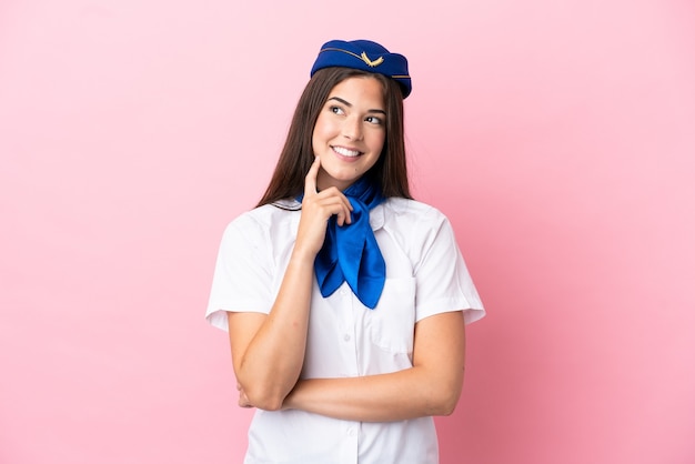 Mulher brasileira aeromoça isolada em fundo rosa pensando uma ideia enquanto olha para cima