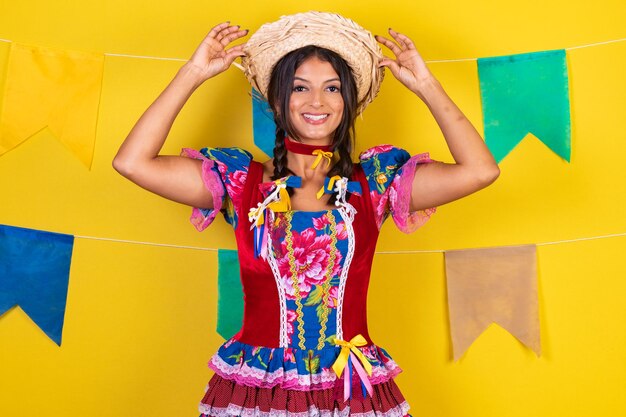 Foto mulher brasileira com roupas da festa de são joao festa junina em fundo amarelo com bandeiras