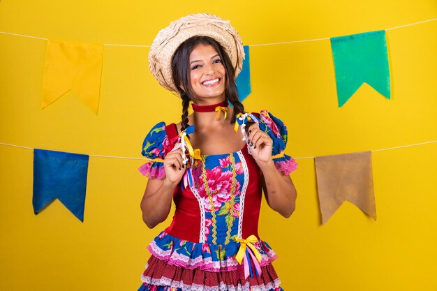 Foto mulher brasileira com roupas da festa de são joao festa junina em fundo amarelo com bandeiras