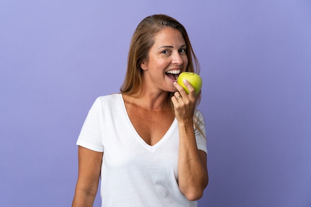 Mulher brasileira de meia-idade isolada em uma parede roxa comendo uma maçã