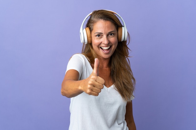 Mulher brasileira de meia-idade isolada na parede roxa ouvindo música e com o polegar para cima