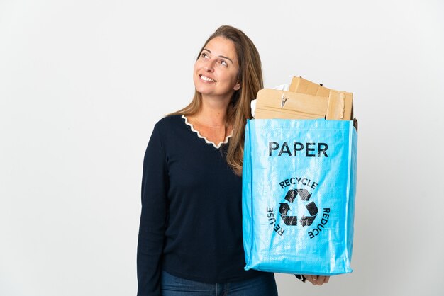 Mulher brasileira de meia-idade segurando uma sacola de reciclagem cheia de papel para reciclar mais isolada pensando uma ideia enquanto olha para cima