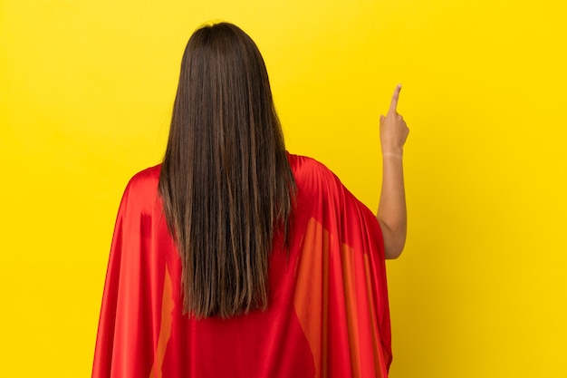 Mulher brasileira super-heroína isolada em fundo amarelo apontando para trás com o dedo indicador