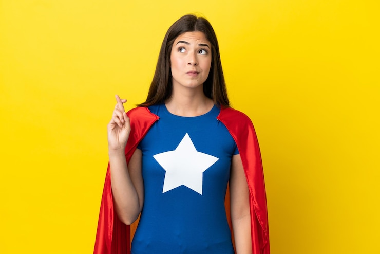 Foto mulher brasileira super-heroína isolada em fundo amarelo com dedos se cruzando e desejando o melhor