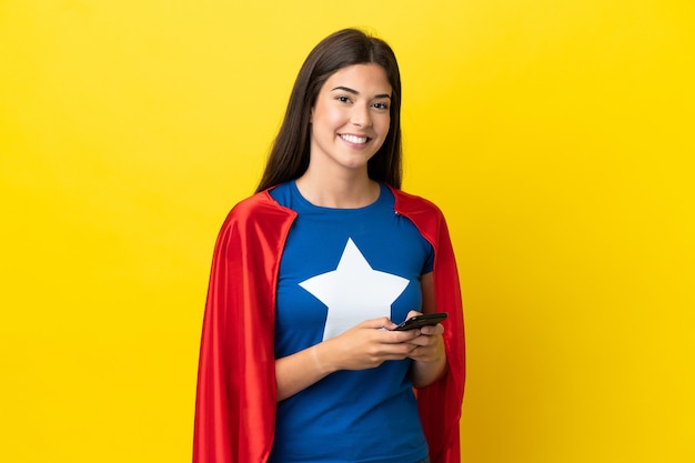 Mulher brasileira super-heroína isolada em fundo amarelo enviando mensagem pelo celular