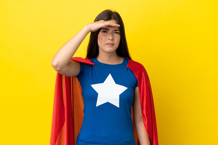 Foto mulher brasileira super-heroína isolada em fundo amarelo olhando para longe com a mão para olhar algo