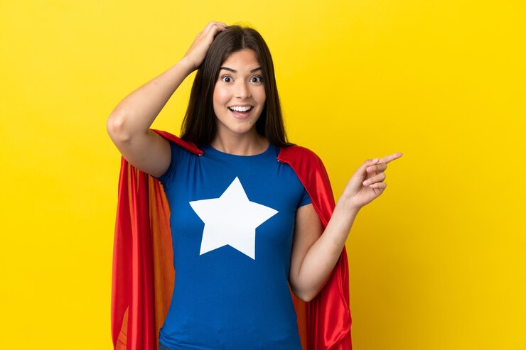 Foto mulher brasileira super-heroína isolada em fundo amarelo surpreendida e apontando dedo para o lado