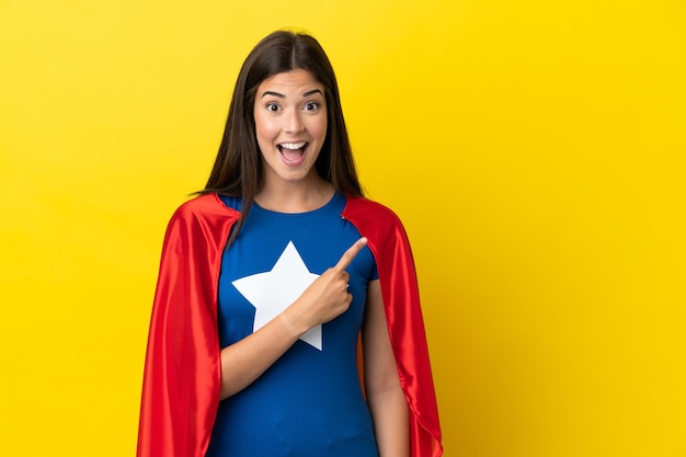 Mulher brasileira super-heroína isolada em fundo amarelo surpreendida e apontando para o lado