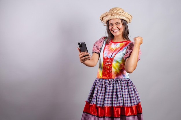 Mulher brasileira vestindo roupas country Festa de São João Festa junina brincando com o smartphone e comemorando