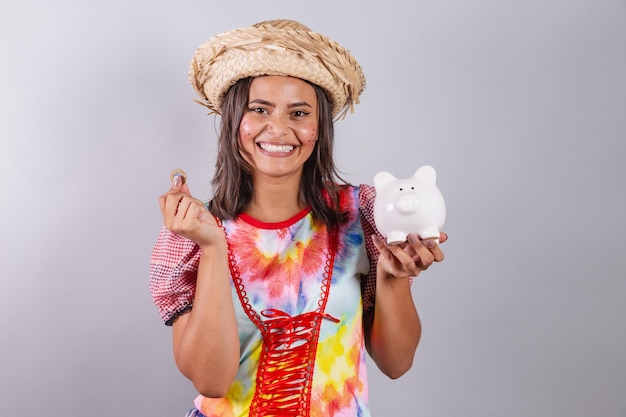 Mulher brasileira vestindo roupas country Festa de São João Festa Junina segurando o cofrinho e a moeda