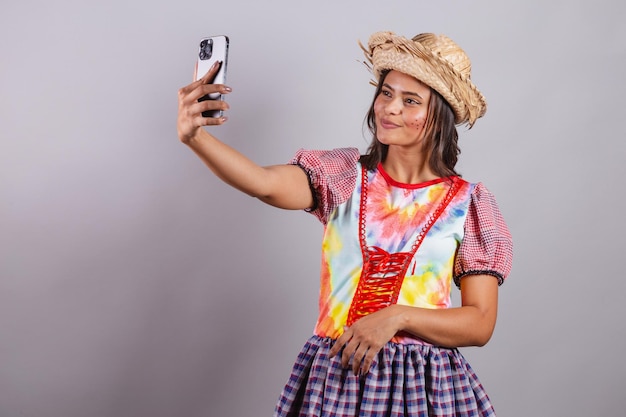 Mulher brasileira vestindo roupas country Festa de São João Festa Junina tirando autorretrato com selfie de smartphone