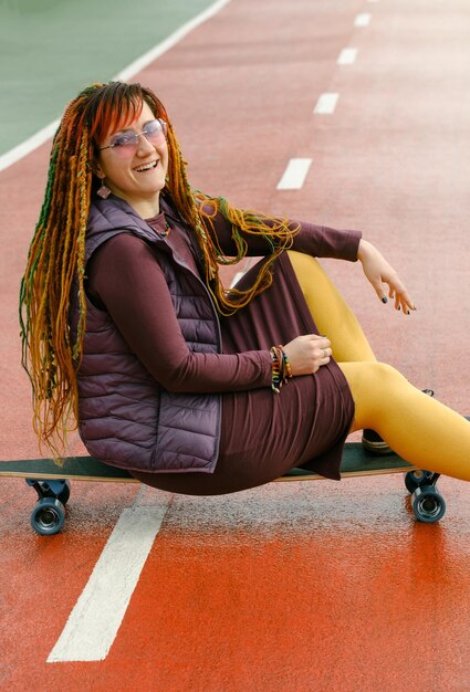 Mulher brilhante com dreadlocks carregando skate na estrada