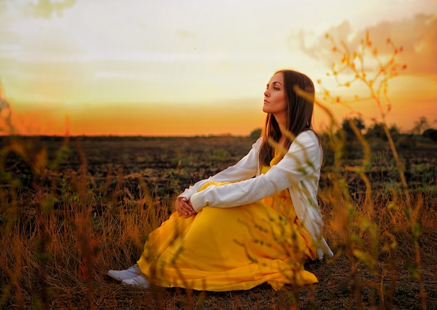 Mulher brilhante relaxa sentado em um campo do sol.