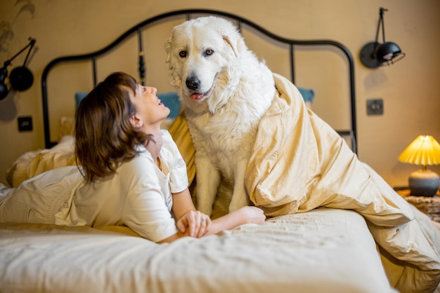 Foto mulher brinca com seu cachorro enquanto está deitada na cama