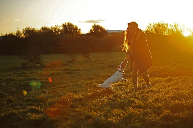 Mulher brincando com cão no campo contra o céu ao pôr do sol