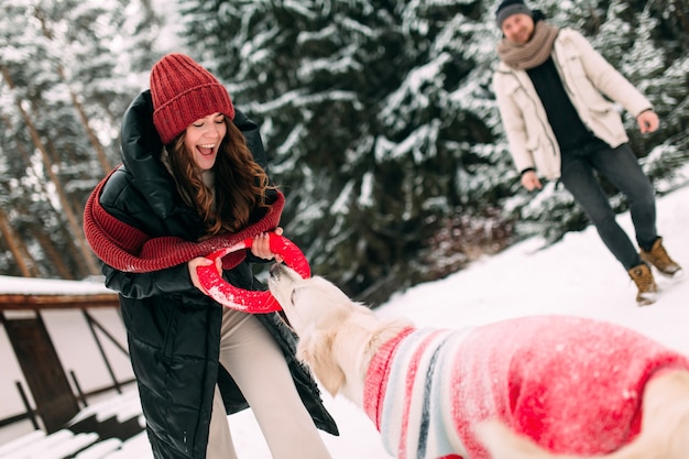 Mulher brincando com um cachorro em uma rua cheia de neve com um donut vermelho