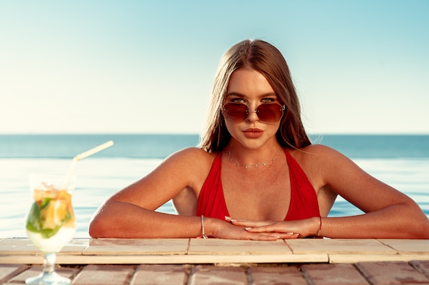 Mulher bronzeada em biquíni vermelho em uma piscina com cocktail