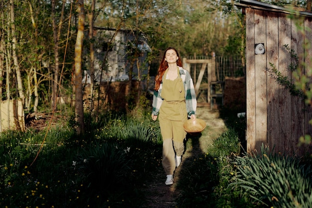 Mulher caminha alegremente pelo jardim com alimentador de pássaros depois de alimentar galinhas em sua fazenda