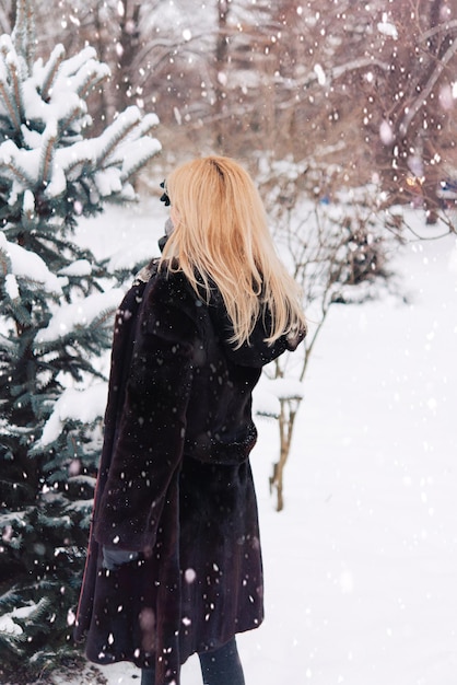 Mulher caminha ao ar livre no inverno. Roupas quentes no tempo frio. Mulher em um casaco de pele e jeans