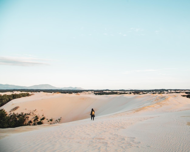 Mulher caminhando na areia contra o céu