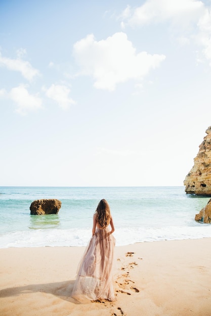 Mulher caminhando na praia contra as rochas e o oceano