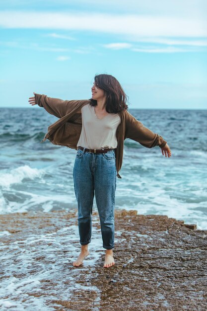 Mulher caminhando pela praia rochosa em jeans molhados com os pés descalços. férias de verão no mar