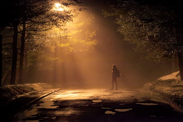 Mulher caminhando sozinha na estrada enevoada e enevoada em uma cena mística dramática com cores quentes