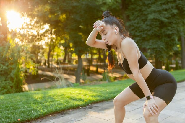 Mulher cansada em roupas esportivas no parque ao nascer do sol