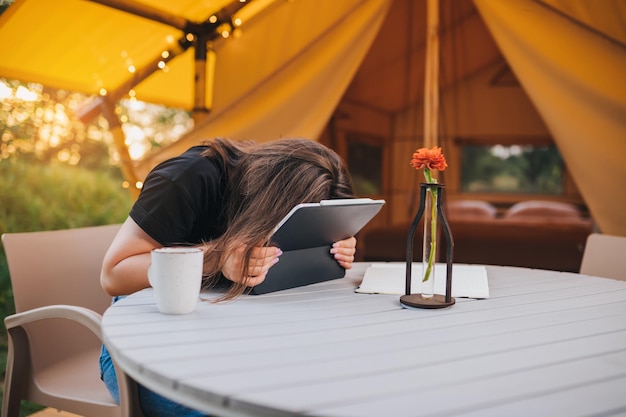 Mulher cansada freelancer usando um laptop em uma barraca de glamping aconchegante em um dia ensolarado Barraca de acampamento de luxo para férias de verão ao ar livre e férias Conceito de estilo de vida