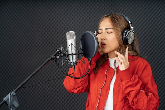 Mulher cantora asiática em um estúdio de gravação usando um microfone de estúdio com paixão em um estúdio de gravação de música