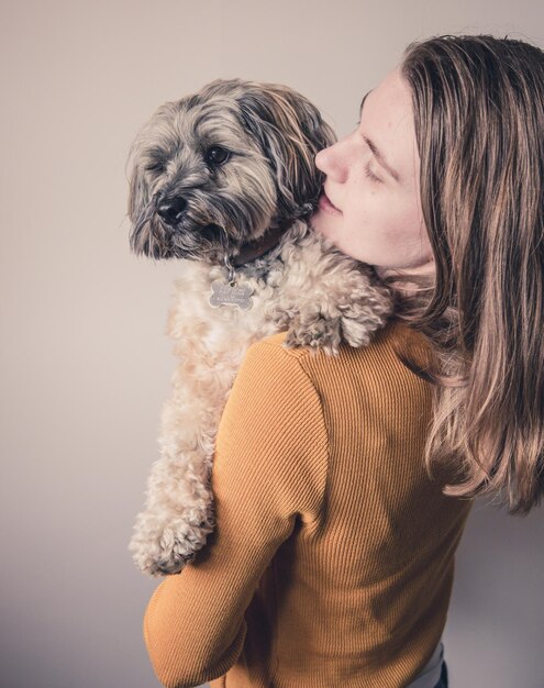 Foto mulher carregando cachorro enquanto está de pé contra a parede