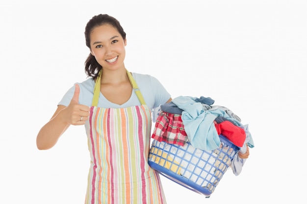 Mulher carregando cesta de roupa e dando polegares para cima