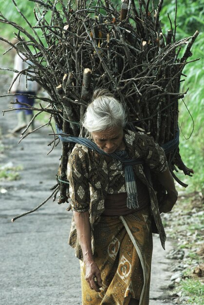 Foto mulher carregando troncos na calçada