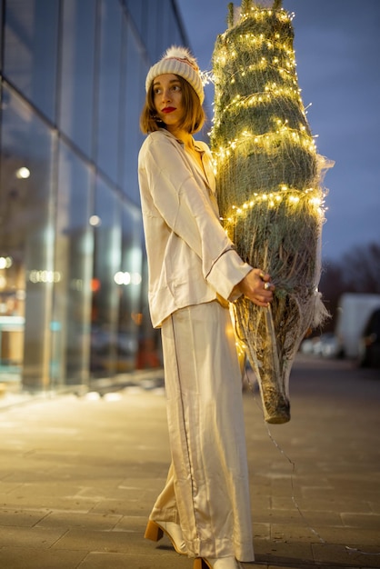 Mulher carregando uma árvore de natal iluminada perto do shopping
