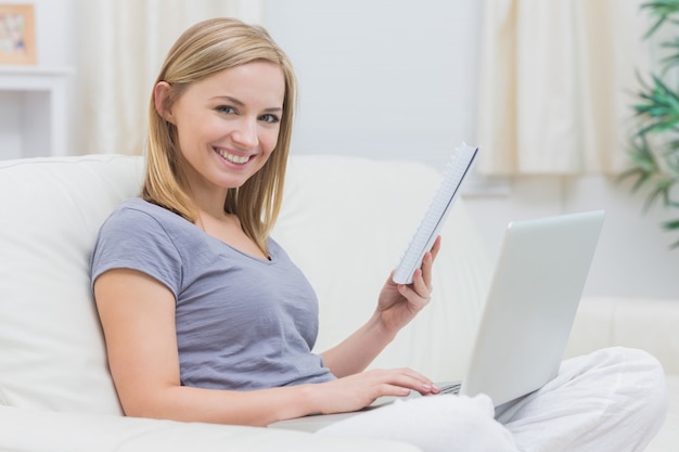 Mulher casual com laptop e livro na sala de estar