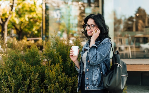 Mulher casual tomando café enquanto conversa no telefone na rua