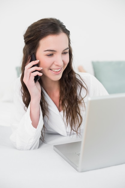 Mulher casual usando celular e laptop na cama