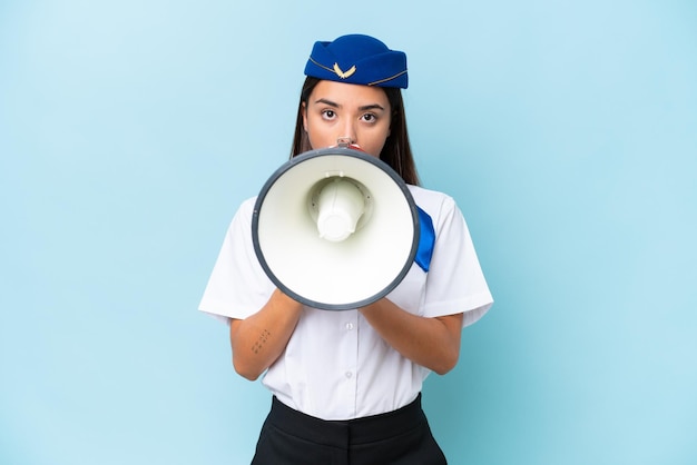 Foto mulher caucasiana aeromoça de avião isolada em fundo azul gritando através de um megafone